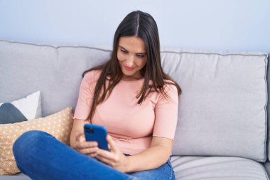 Evdeki kanepede oturan akıllı telefon kullanan genç, güzel İspanyol kadın.