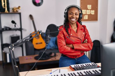 Müzik stüdyosunda kollarını kavuşturup gülümseyen Afrikalı Amerikalı kadın müzisyen.