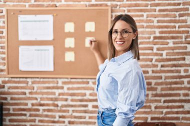 Genç, güzel, İspanyol bir iş adamı ofisteki mantar tahtaya yazı yazıyor.