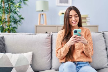 Evdeki kanepede oturan akıllı telefon kullanan genç, güzel İspanyol kadın.