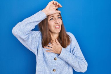 Young woman standing over blue background touching forehead for illness and fever, flu and cold, virus sick 