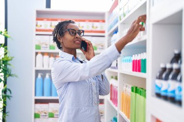 Middle age african american woman customer smiling confident talking on smartphone at pharmacy