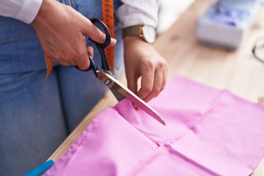 Dikiş atölyesinde kumaş kesen genç bir kadın.