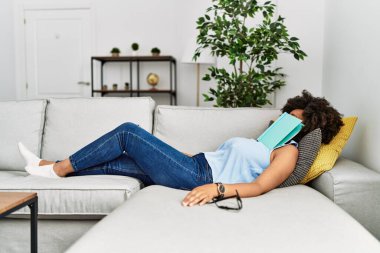 Genç Afrikalı Amerikalı kadın evde kitapla uyuyor.