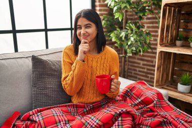 Kanepede oturup kahve içen genç İspanyol kadın bir soru hakkında endişeli ve gergin bir şekilde düşünüyor. 