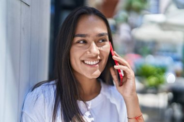 Genç, güzel, İspanyol bir kadın gülümsüyor ve caddede akıllı telefondan konuşuyor.