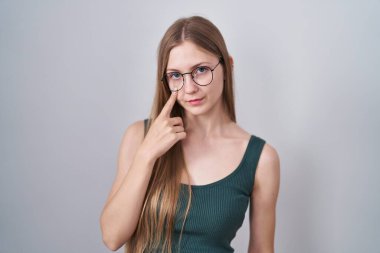 Young caucasian woman standing over white background pointing to the eye watching you gesture, suspicious expression 