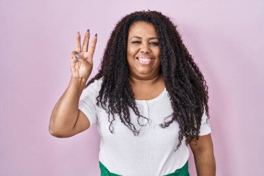 Plus size hispanic woman standing over pink background showing and pointing up with fingers number three while smiling confident and happy. 
