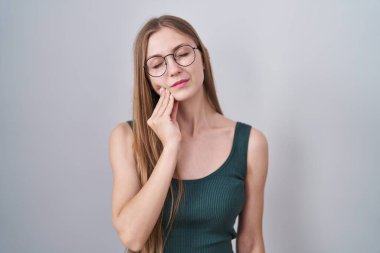 Young caucasian woman standing over white background touching mouth with hand with painful expression because of toothache or dental illness on teeth. dentist 