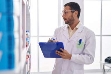 Young man pharmacist writing on document organize shelving at pharmacy