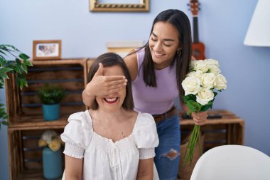 Two women mother and daughter surprise with bouquet of flowers at home