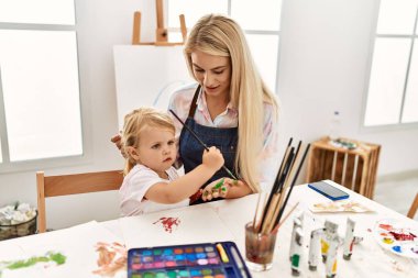 Mother and daughter smiling confident painting palm hands at art studio
