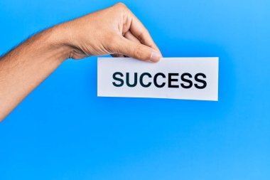 Hand of caucasian man holding paper with success word over isolated blue background