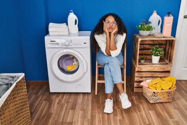 Çamaşırhanede çamaşır makinesini bekleyen genç, sıkıcı Latin kadın.