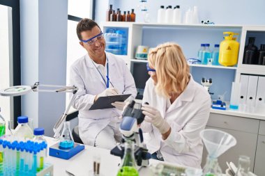 Middle age man and woman scientist partners working using microscope at laboratory