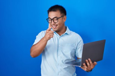 Chinese young man using computer laptop pointing fingers to camera with happy and funny face. good energy and vibes. 