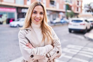 Sokakta kollarını kavuşturmuş genç sarışın kadın.