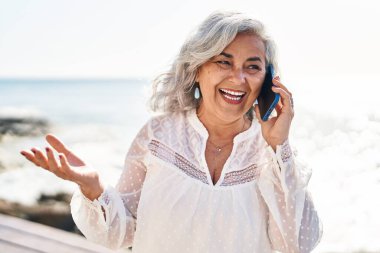 Orta yaşlı bir kadın deniz kenarında akıllı telefondan konuşarak kendine güveniyor.