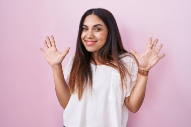Young arab woman standing over pink background showing and pointing up with fingers number ten while smiling confident and happy. 