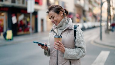 Orta yaşlı İspanyol kadın akıllı telefon kullanıyor. Sokakta kahve içiyor.