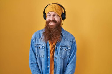 Uzun sakallı, müzik dinleyen, kulaklık takan, kameraya seksi bir ifadeyle bakan, neşeli ve mutlu yüzlü beyaz bir adam.. 