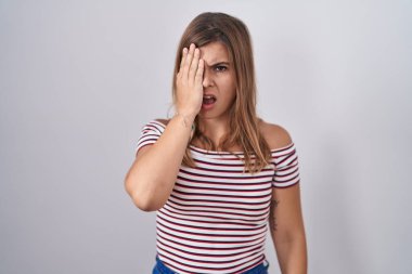 Young hispanic woman standing over isolated background yawning tired covering half face, eye and mouth with hand. face hurts in pain. 
