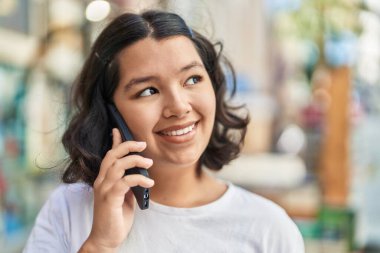 Gülümseyen genç bir kadın caddedeki akıllı telefondan konuşuyor.