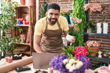 Young arab man florist using laptop holding plant at florist