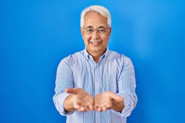 Elleri avuçlarında gülümseyen gözlüklü İspanyol kıdemli adam el hareketi yapıyor ya da yapıyor. Bekleme ve koruma 