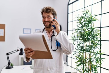 Doktor üniforması giyen genç İspanyol adam klinikteki akıllı telefondan konuşuyor.