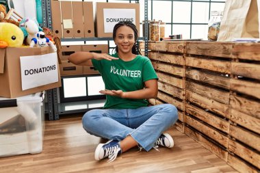 Young african american woman wearing volunteer t shirt at donations stand gesturing with hands showing big and large size sign, measure symbol. smiling looking at the camera. measuring concept. 