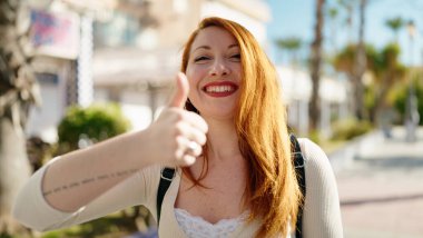 Young redhead woman smiling confident doing ok sign with thumb up at park