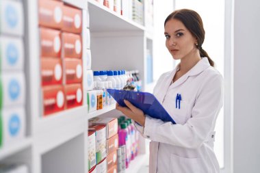 Young woman pharmacist writing on clipboard at pharmacy