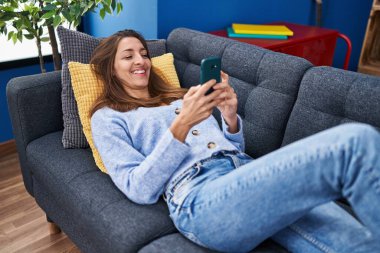 Genç kadın evde koltukta yalan smartphone kullanarak