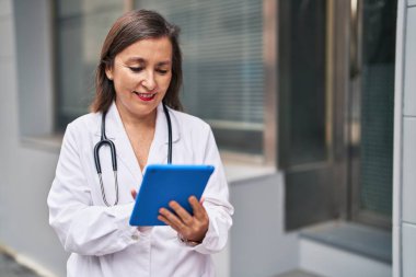 Middle age woman wearing doctor uniform using smartphone at street