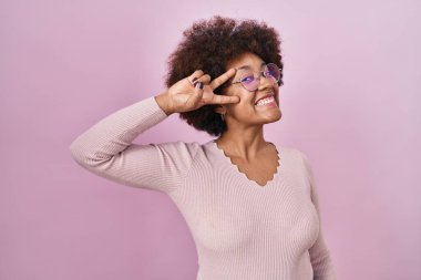 Pembe arka planda duran genç Afro-Amerikan kadın barış sembolü yapıyor. Yüzünde parmakları, gülümseyerek zaferini gösteriyor. 