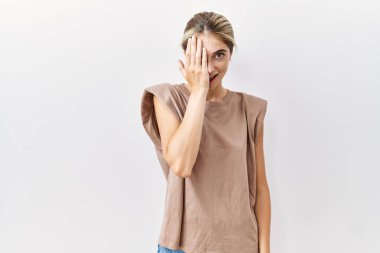 Sarışın genç bir kadın izole edilmiş arka planda duruyor. Bir gözünü eliyle kapatıyor. Yüzünde kendine güvenen bir gülümseme ve şaşırtıcı bir duygu var.. 