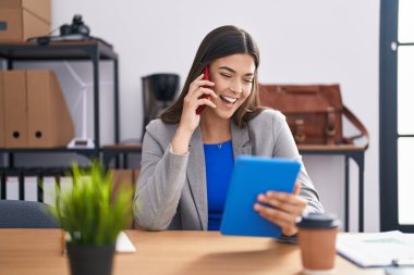 Genç, güzel İspanyol iş kadını. Ofiste dokunmatik ped kullanarak akıllı telefondan konuşuyor.