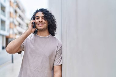 Genç Latin adam gülümsüyor. Kendine güveniyor. Akıllı telefondan konuşuyor.