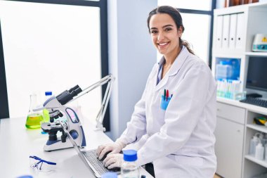 Laboratuvarda dizüstü bilgisayar kullanan Latin kökenli genç bir kadın.