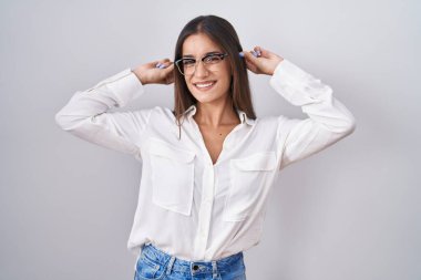 Young brunette woman wearing glasses smiling pulling ears with fingers, funny gesture. audition problem 