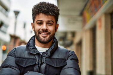 Kasabada çapraz kollarla gülümseyen genç bir Arap.