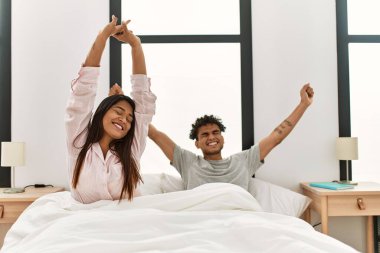 Genç Latin çift, yatak odasındaki yatakta esniyor ve kollarını uzatıyor..
