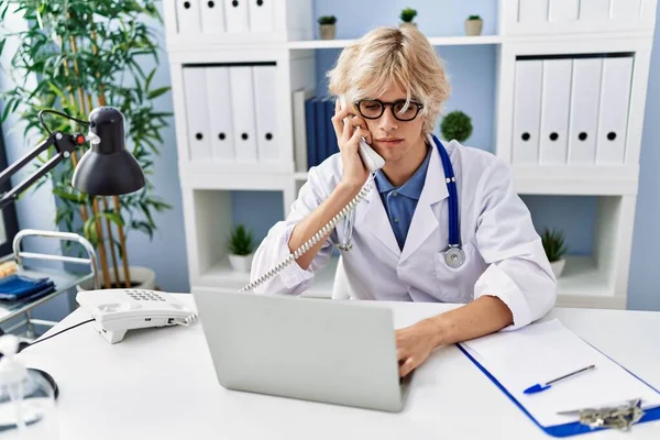 Молодий Блондинка Лікар Використовує Ноутбук Розмовляючи Телефону Клініці — стокове фото