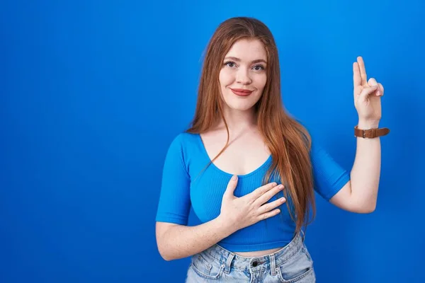 Mulher Ruiva Sobre Fundo Azul Sorrindo Jurando Com Mão Peito — Fotografia de Stock