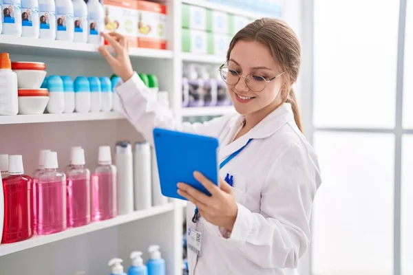 若いブロンドの女性薬剤師が薬局で薬を探しているタッチパッドを使用して — ストック写真