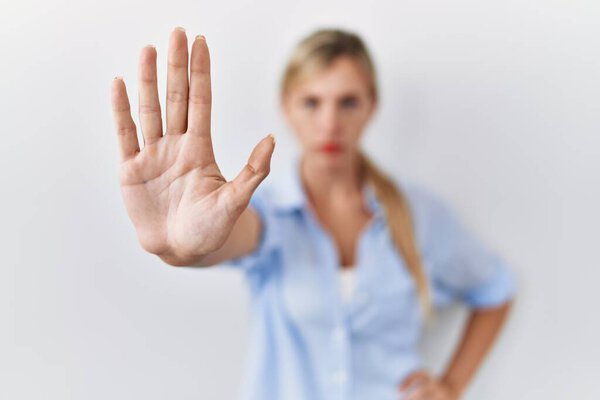 Beautiful blonde woman standing over white background doing stop sing with palm of the hand. warning expression with negative and serious gesture on the face. 