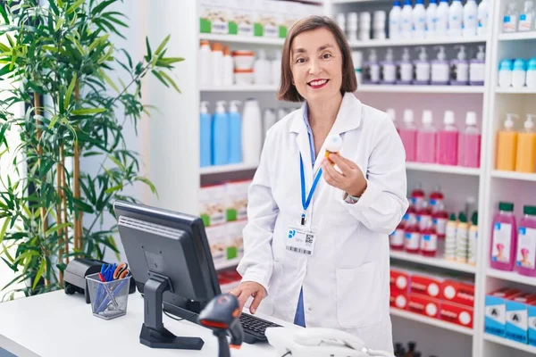 薬局で薬瓶を保持しているコンピュータを使用した中年女性薬剤師 — ストック写真