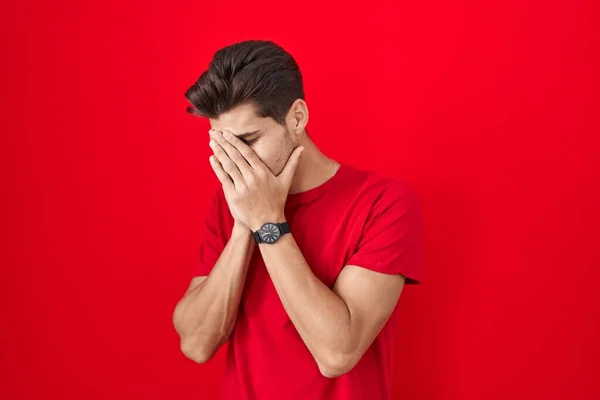 泣きながら手で顔を覆う悲しい表情で赤い背景の上に立つ若いヒスパニック系の男 うつ病の概念 — ストック写真