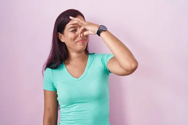 ピンク色の背景の上に立つ若いヒスパニック系の女性は 鼻の上に指で息を保持し 臭いと嫌な 耐え難い匂いを嗅ぐ 臭いが悪い — ストック写真